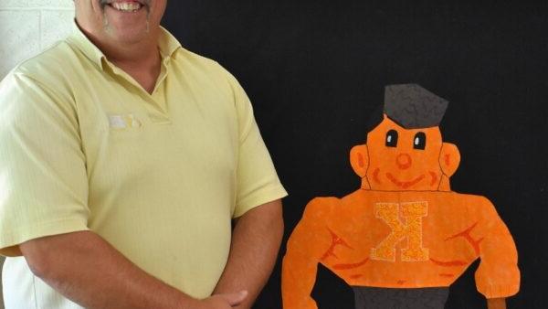 Kewanee High School teacher standing in front of a quilt featuring the school's mascot, a boilermaker